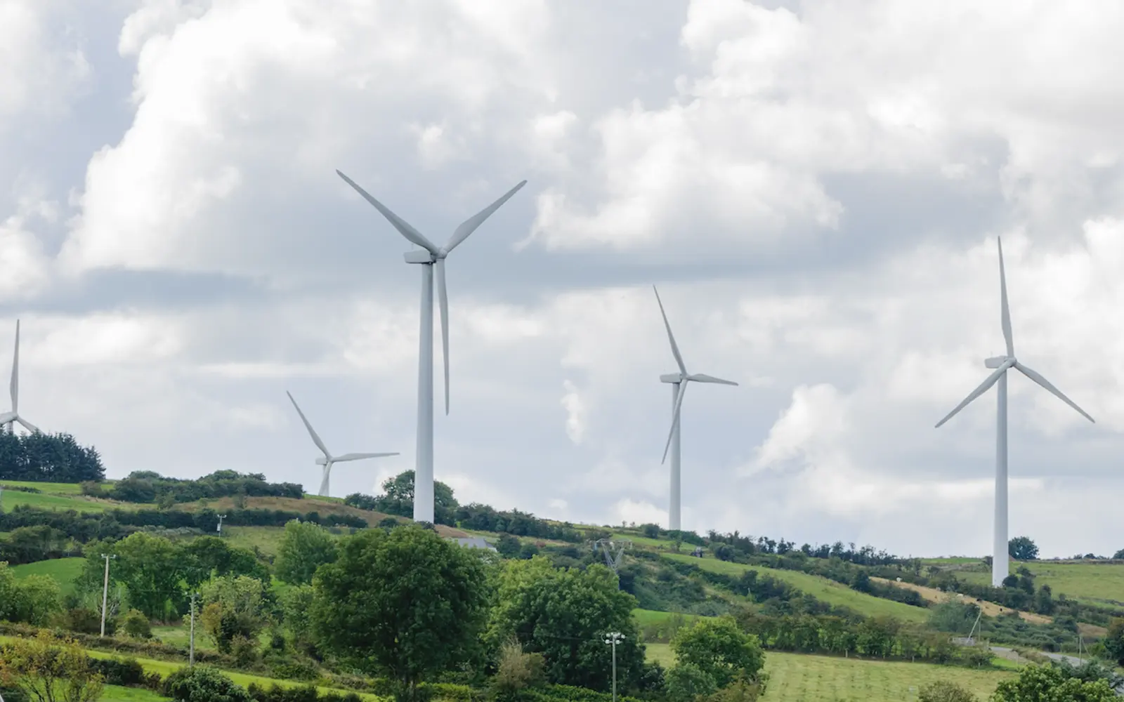 A landscape featuring multiple wind turbines on rolling green hills under a partly cloudy sky.