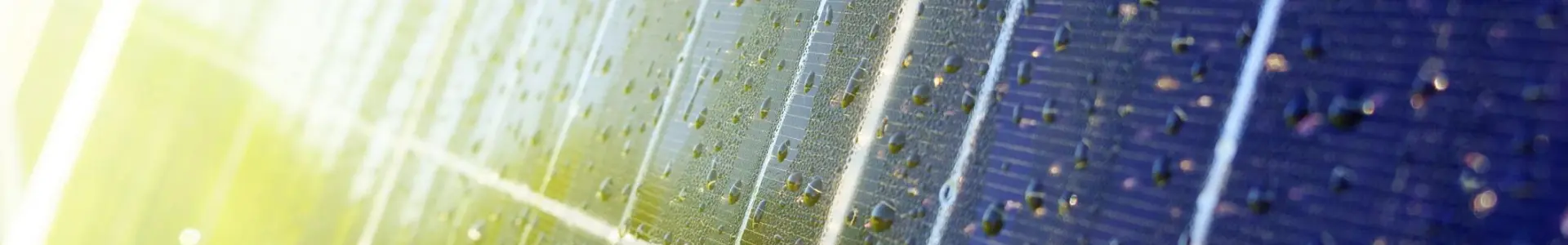 Close-up view of a solar panel surface with water droplets, reflecting sunlight, and green grass in the background.