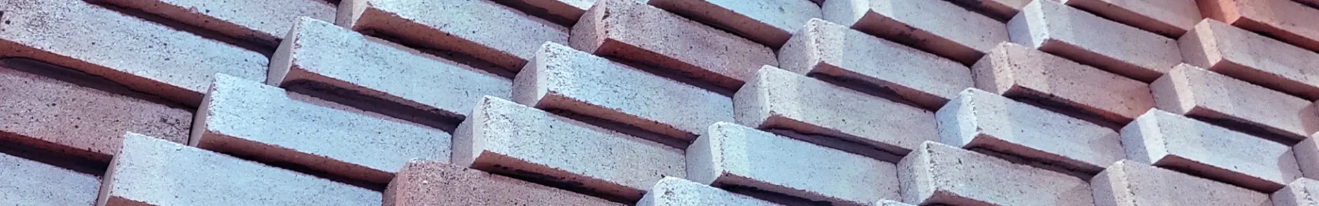 A close-up of a textured wall made of interlocking bricks arranged in a diagonal pattern, showcasing various shades of red and gray.