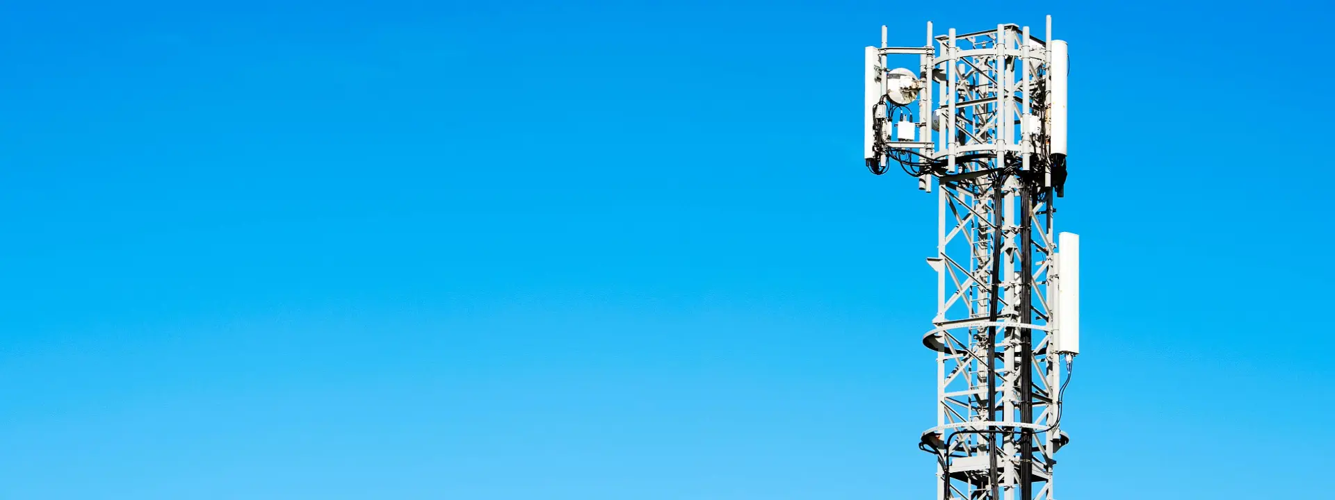 A telecommunications tower against a clear blue sky. The tower features various antennas and equipment mounted on a metal structure.