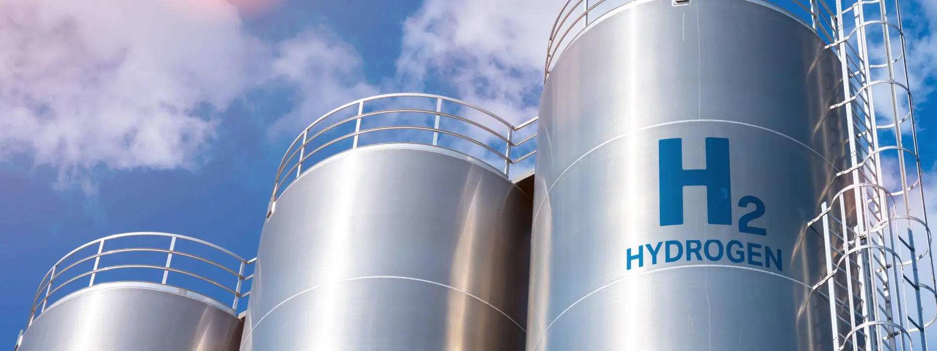 Several large metallic tanks labeled 'H2' and 'HYDROGEN' against a clear blue sky, with some clouds visible.
