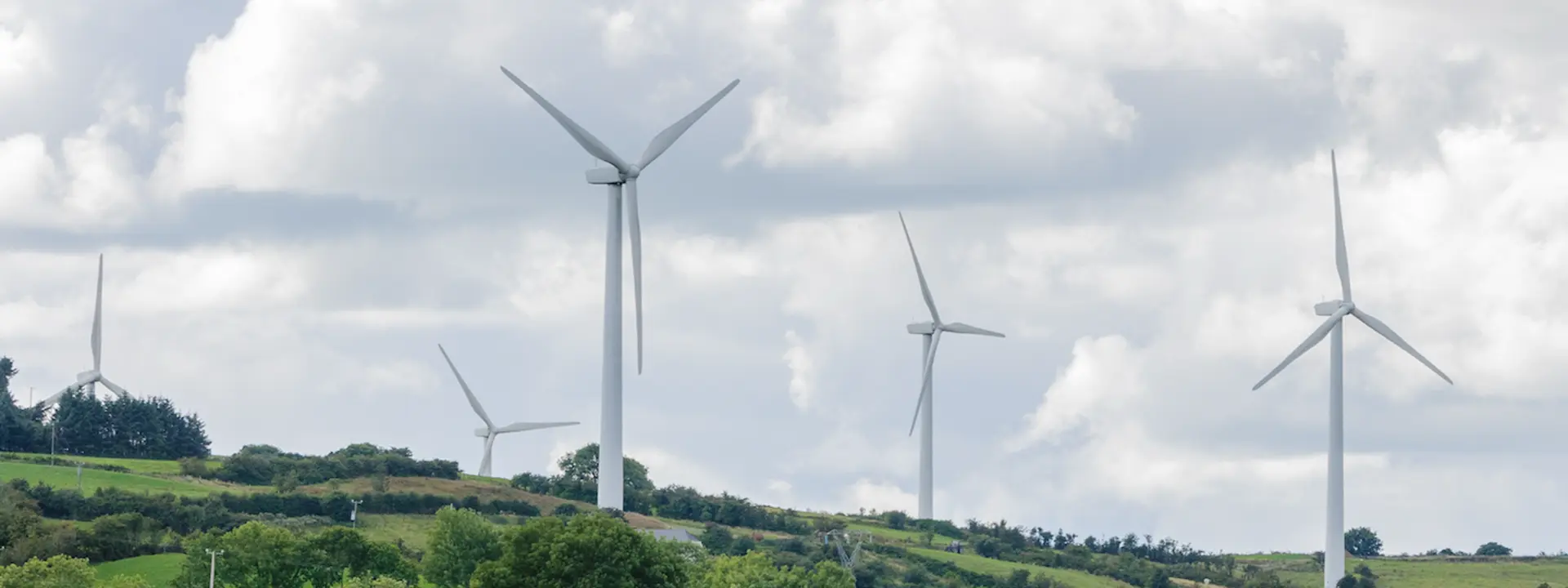 A landscape featuring multiple wind turbines on rolling green hills under a partly cloudy sky.