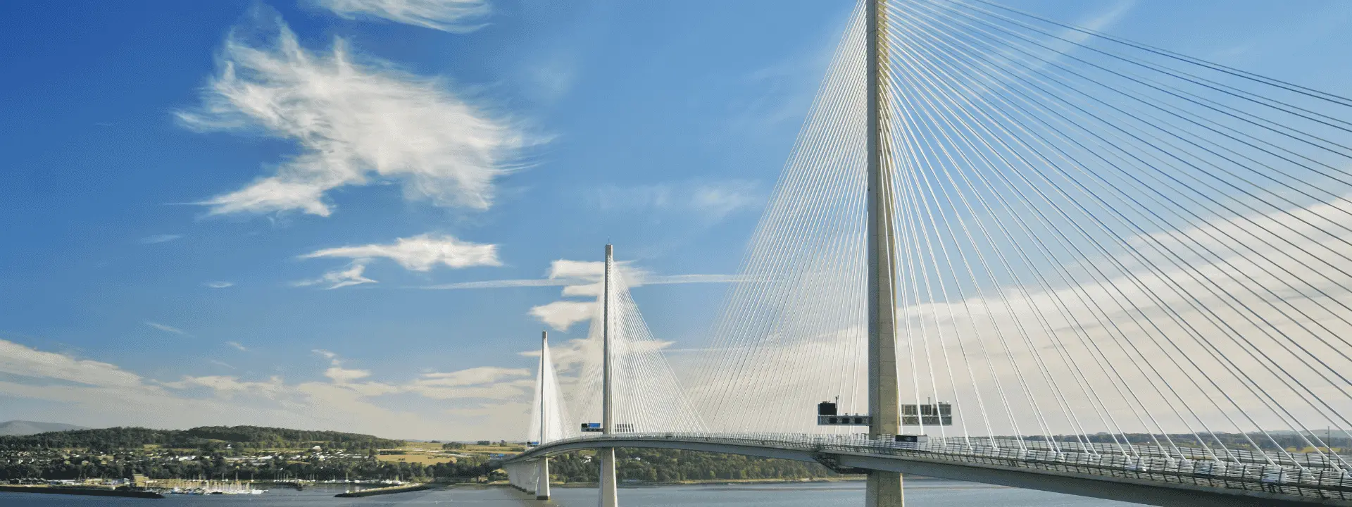 A modern cable-stayed bridge spanning a river with a blue sky and scattered clouds above. The bridge features tall pylons and a smooth roadway connecting both sides.