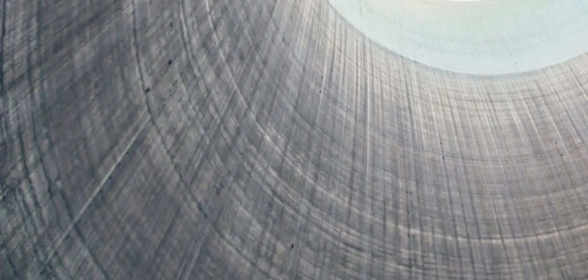 The interior of a large cooling tower with smooth, curved concrete walls. Light streams down from the open top, creating a pattern of shadows on the interior surface.