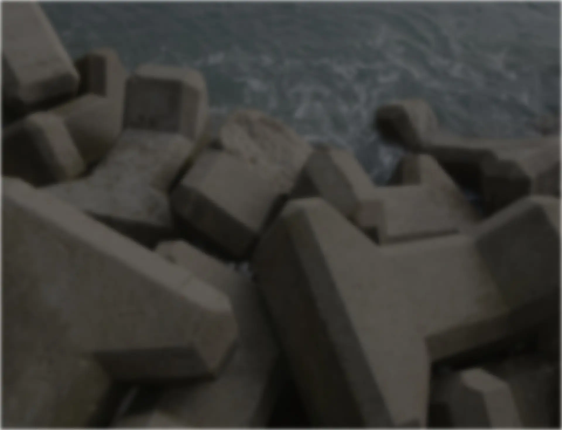 Concrete blocks piled on the edge of a body of water, partially submerged in waves.