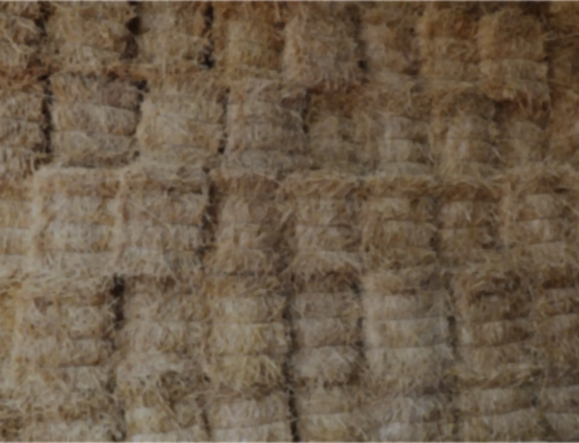A close-up view of compressed straw bales stacked together, showing a textured surface with a beige color and visible strands of straw.