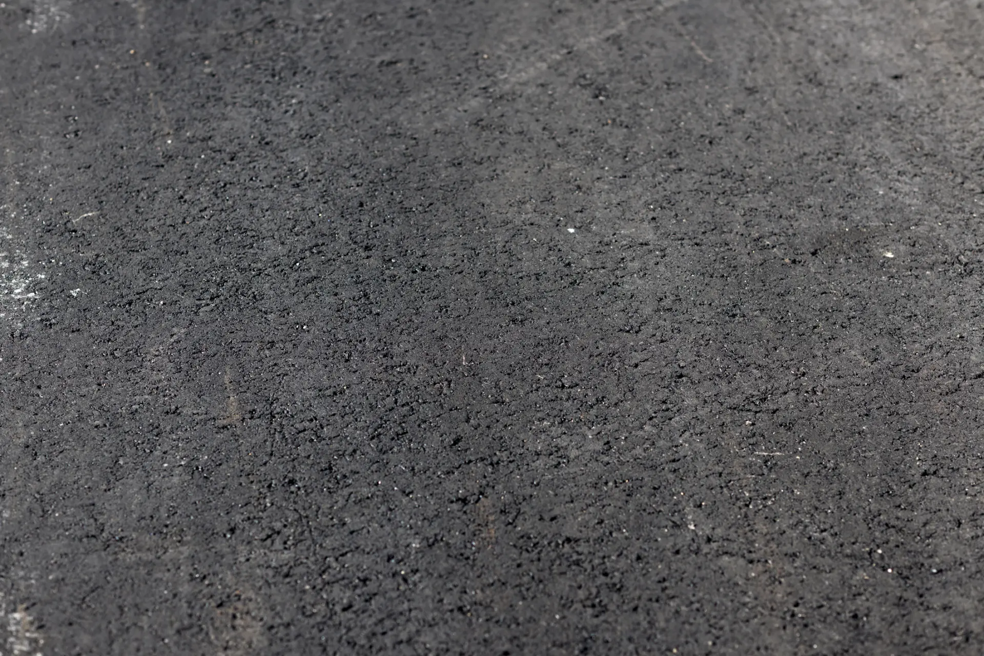 Close-up view of a textured black asphalt surface, showing small pebbles and a rough finish.