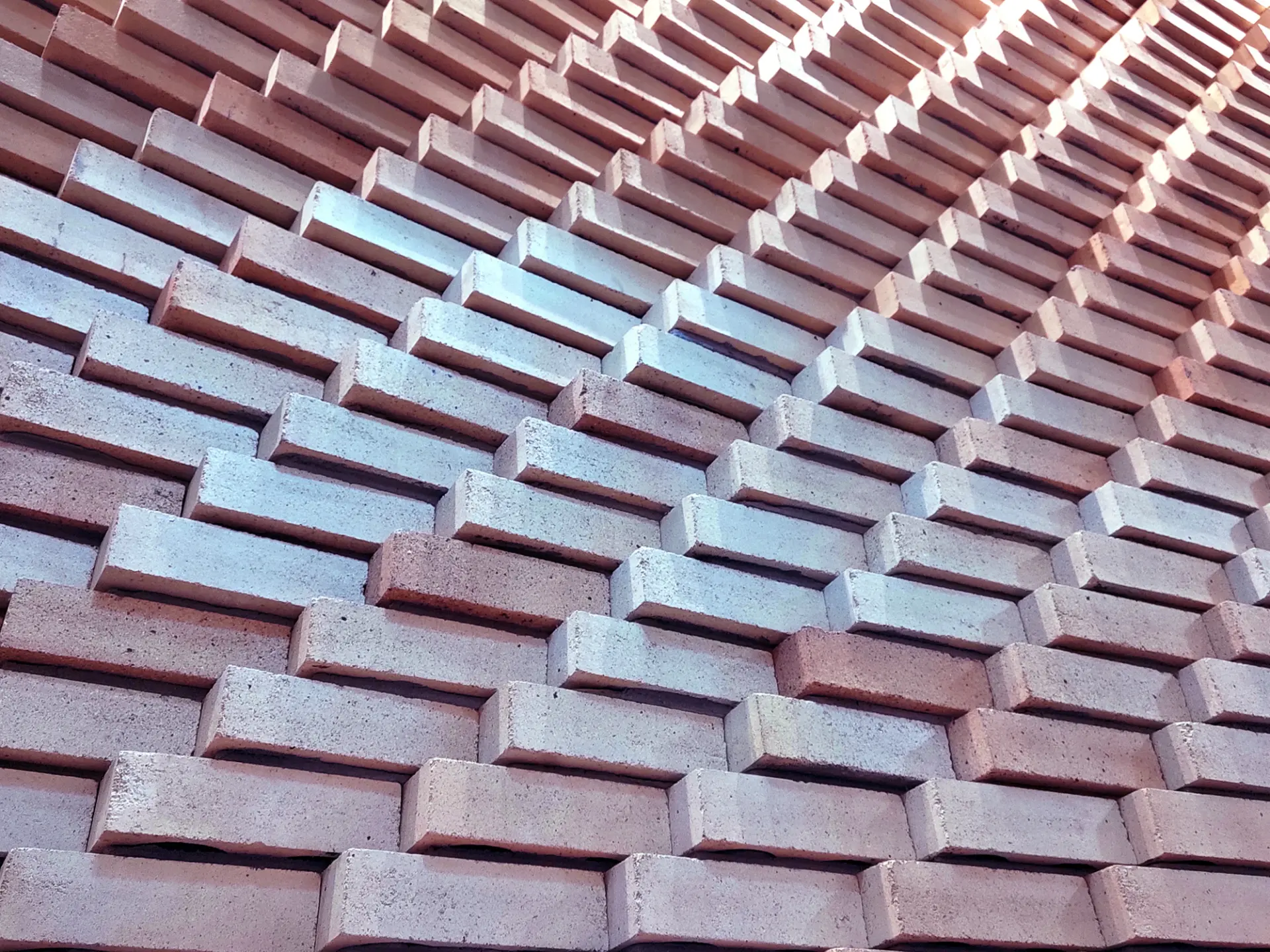 A close-up of a textured wall made of interlocking bricks arranged in a diagonal pattern, showcasing various shades of red and gray.