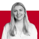 A woman with long blonde hair and a bright smile wearing a white shirt, posing in front of a red background.