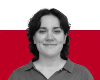 A woman with short dark hair wearing a collared shirt stands against a white and red background.