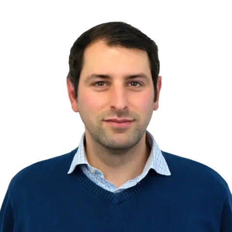 A man with short dark hair, wearing a blue sweater over a light blue collared shirt, is looking directly at the camera with a neutral expression against a transparent background.