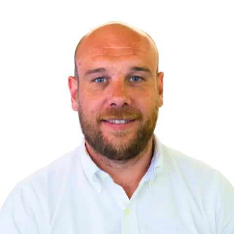 A man with a beard and short hair smiling at the camera, wearing a white collared shirt. The background is plain.