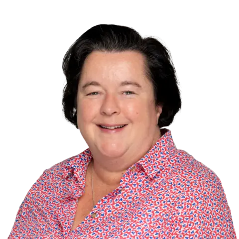 A woman with shoulder-length dark hair smiles at the camera. She wears a red floral blouse and appears in front of a plain white background.