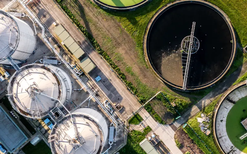 An aerial view of industrial storage tanks and processing facilities, featuring circular tanks with varying contents and green grass surrounding the area.