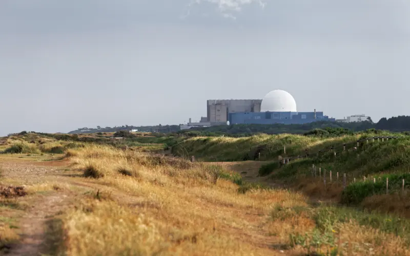 A nuclear power plant with a large white dome in the background, surrounded by grassy terrain and a sandy path leading through the landscape.