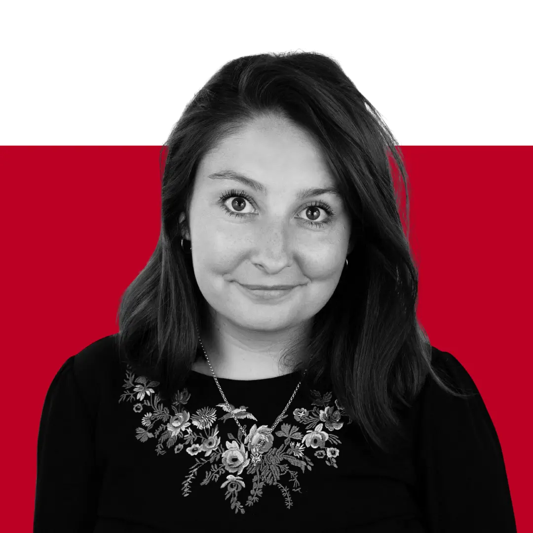A woman with shoulder-length hair, wearing a dark outfit with floral embroidery, is posing against a black and red background.