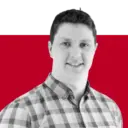 A person in a checked shirt smiling at the camera, set against a red and black background.