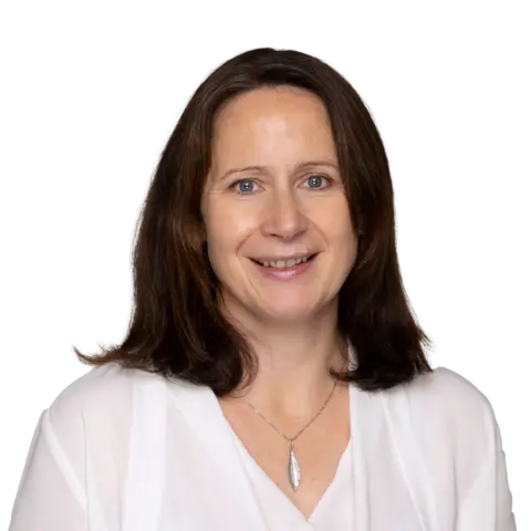 A woman with shoulder-length brown hair wearing a white blouse and a pendant necklace, smiling at the camera against a plain background.