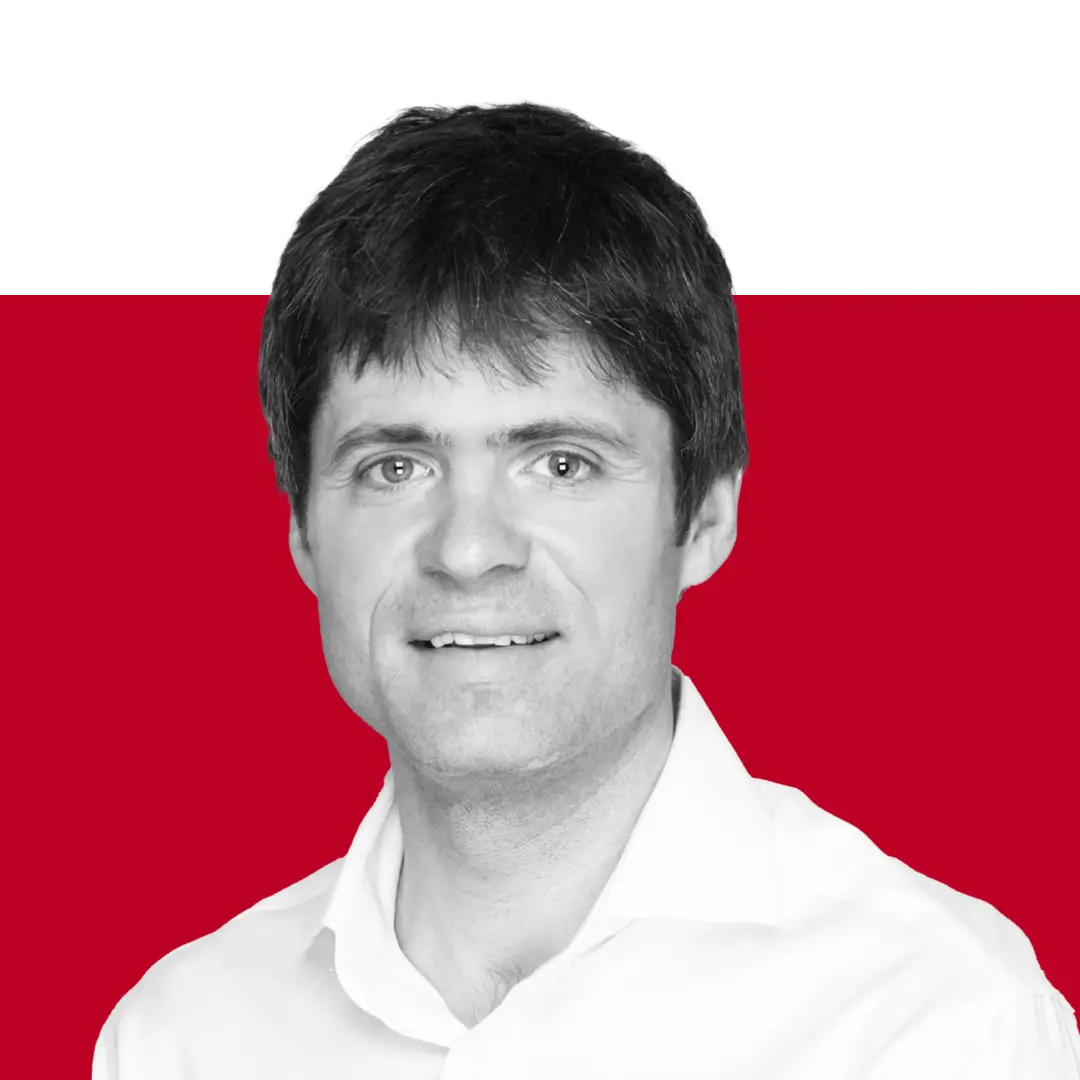 A headshot of a man with short dark hair wearing a white shirt. The background features a gradient of black and red.