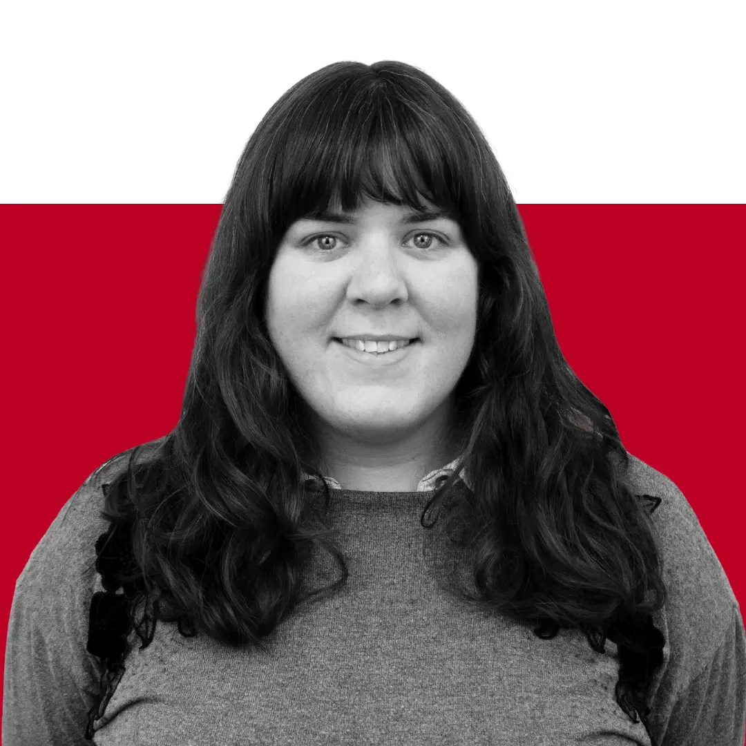 A woman with long dark hair and a gray top smiling in front of a red and black background.