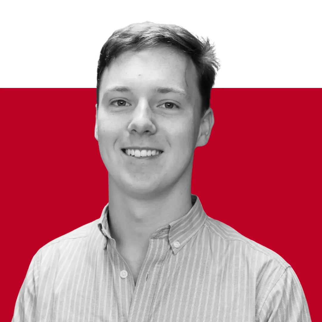 A young man smiling, wearing a button-up shirt, in front of a simple red and black background.