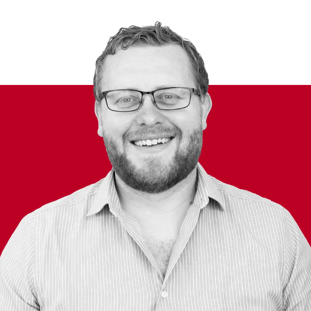 A smiling man with glasses and a beard wearing a collared shirt, set against a red and black background.