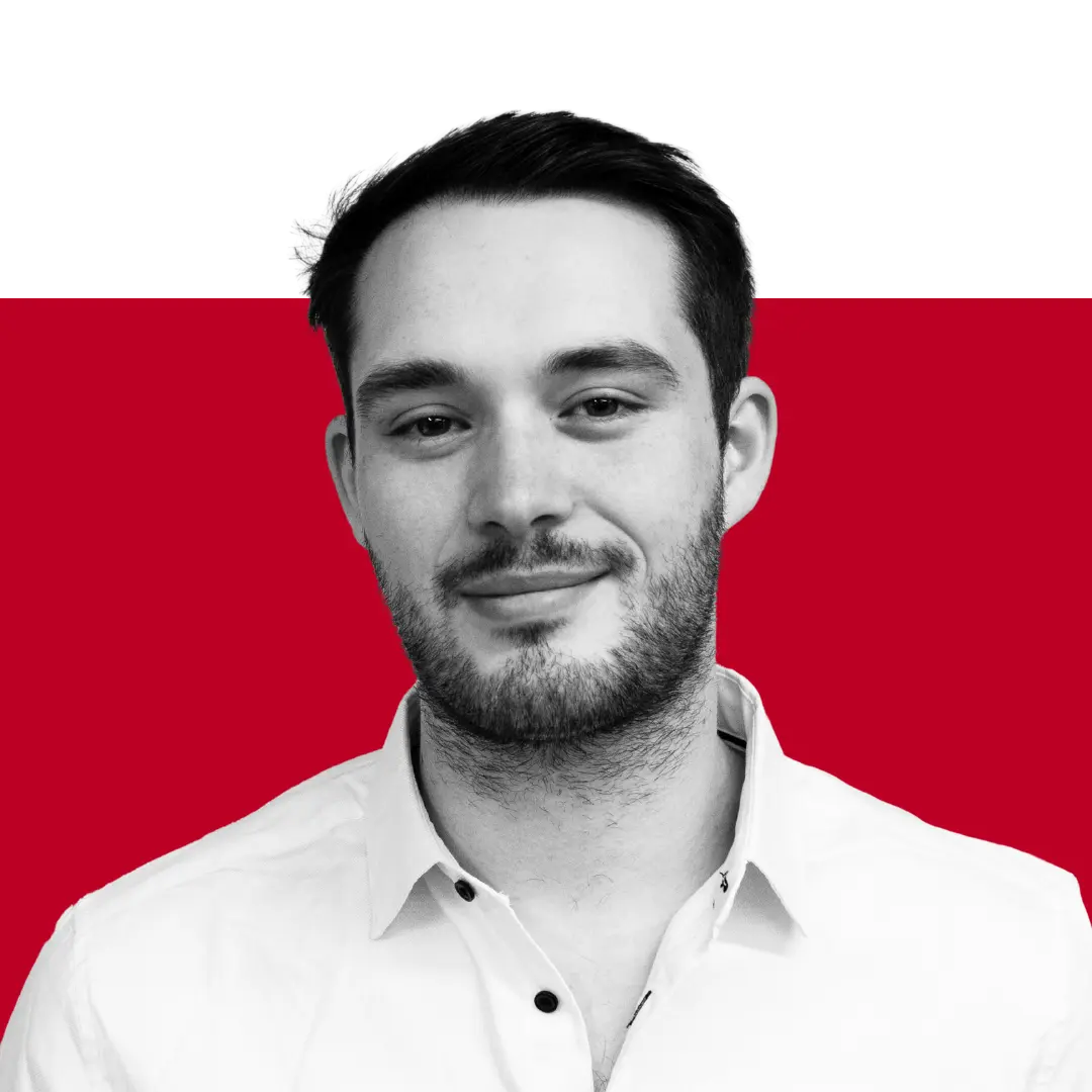 A man with short dark hair and a beard smiling, wearing a white button-up shirt, with a black and red background.