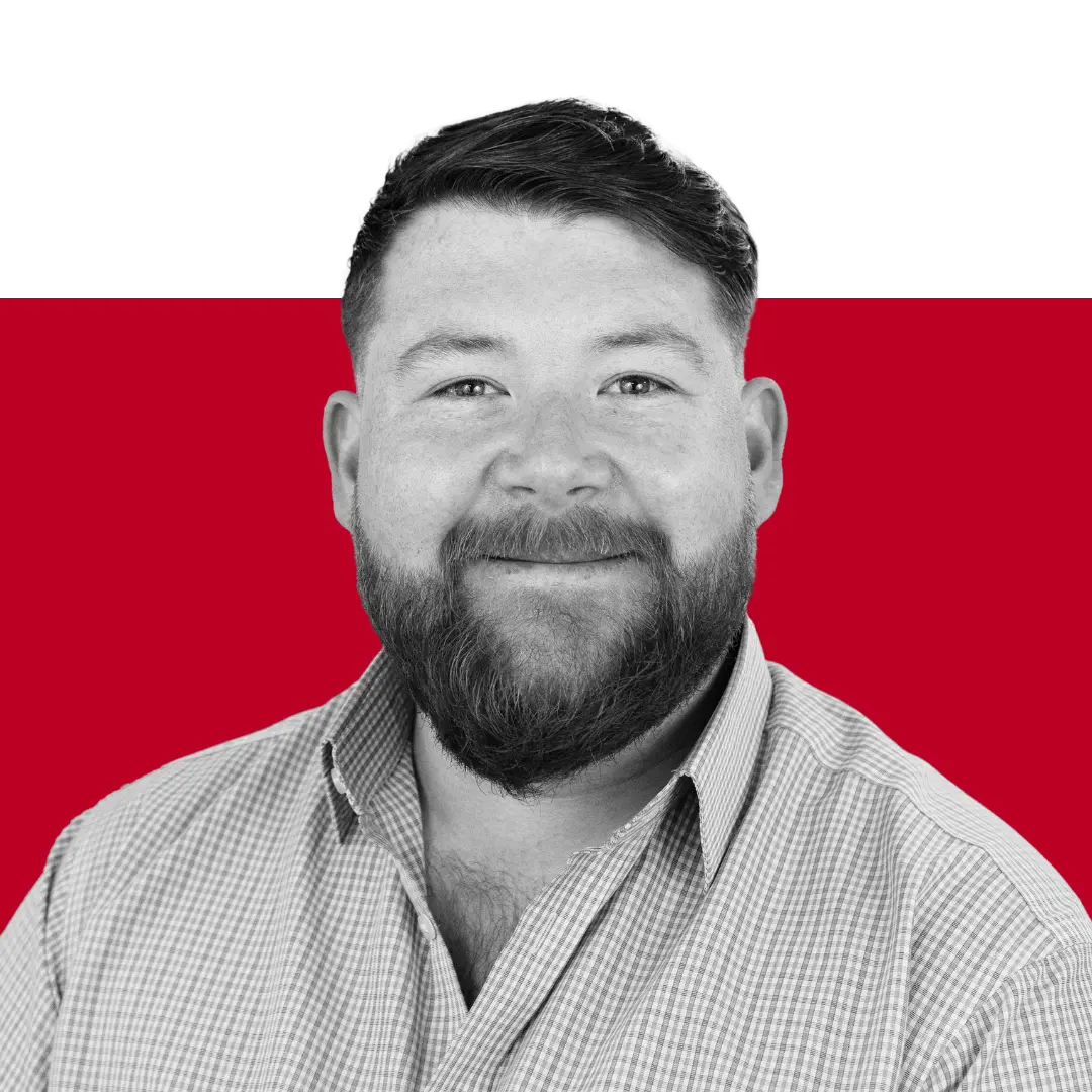 A man with a beard wearing a checkered shirt, smiling at the camera. The background features solid colors, predominantly red and black.