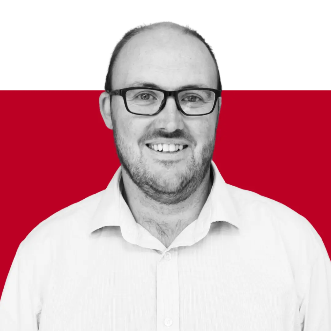 A smiling man with glasses wearing a white collared shirt, set against a red and black background.