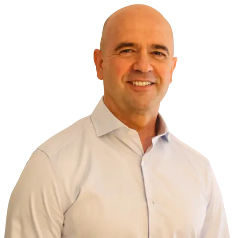 A man smiling while wearing a light blue button-up shirt, standing against a plain white background.