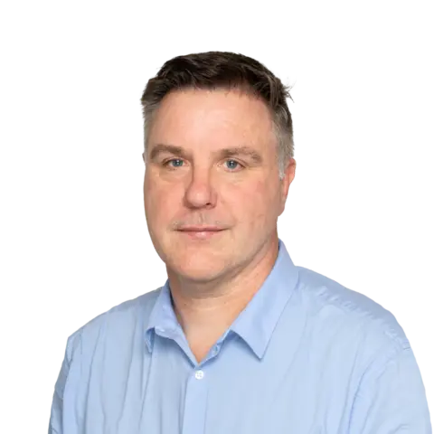 A man with short brown hair and a slight smile, wearing a light blue collared shirt, facing the camera against a white background.