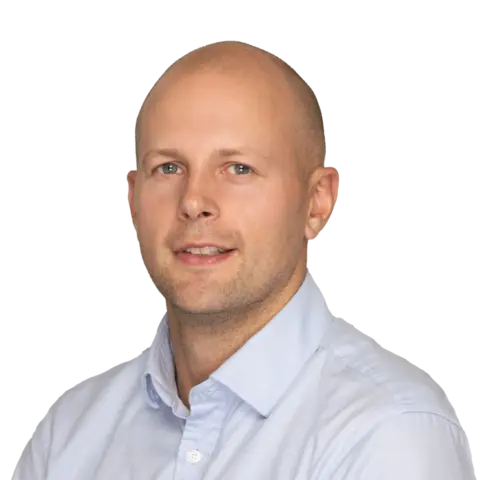 A professional portrait of a man with a shaved head wearing a light blue button-down shirt, smiling against a white background.