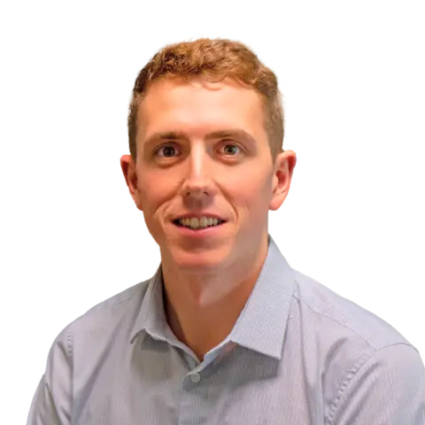 A man with short, light brown hair wearing a light blue button-up shirt, smiling while facing the camera. The background is transparent.