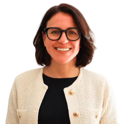 A woman with shoulder-length dark hair wears glasses and a light-colored cardigan over a dark top, smiling at the camera against a plain background.