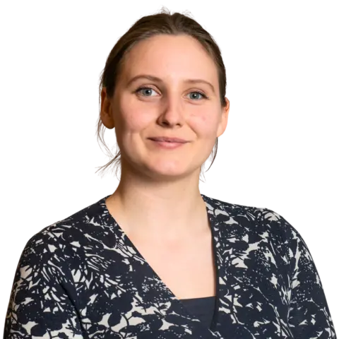 A woman with light brown hair in a floral-patterned cardigan poses for a portrait. She has a neutral expression and is looking directly at the camera against a plain background.
