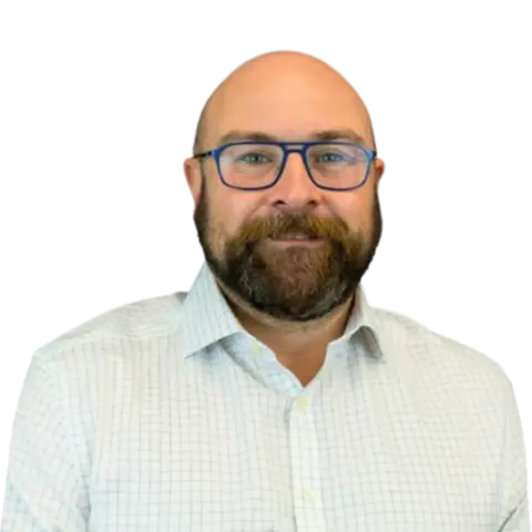 A man with a beard wearing glasses and a checkered shirt, looking directly at the camera with a neutral expression against a transparent background.