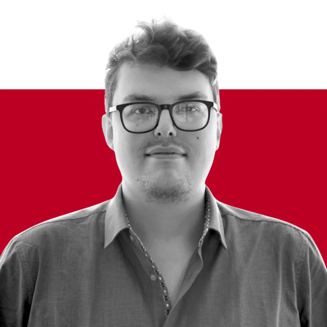 A man with glasses wearing a button-up shirt, standing against a background with a gradient of red and black colors.